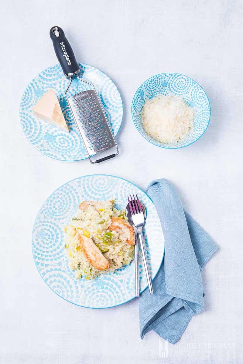 A plate of chicken and leek risotto with grated cheese next to it 