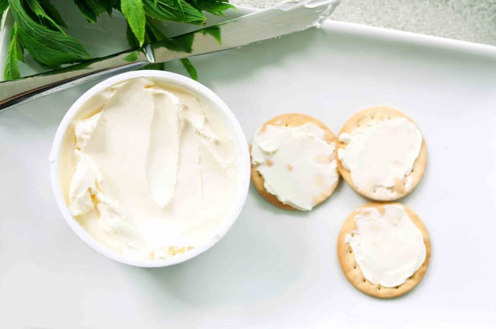 Bowl of cream cheese and three crackers with cream cheese spread.