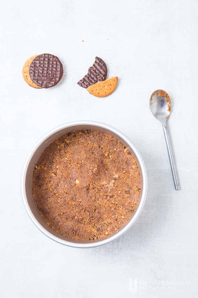 Two chocolate biscuits next to a pan filled with crushed biscuits