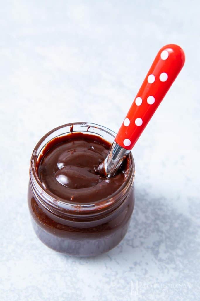 A jar of chocolate fudge sauce with a spoon in it 