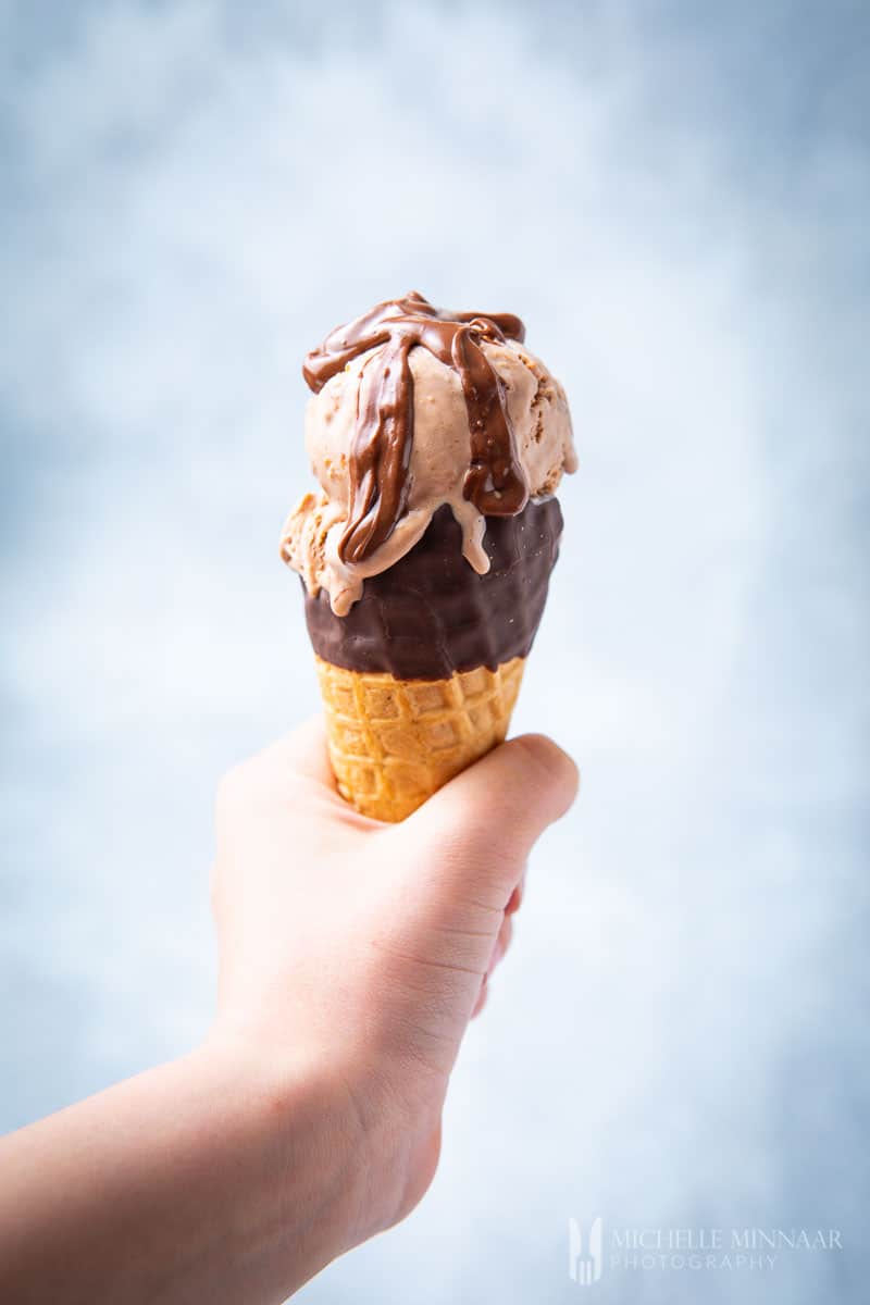 A child's hand holding a a cone with a scoop of ferrero rocher ice cream