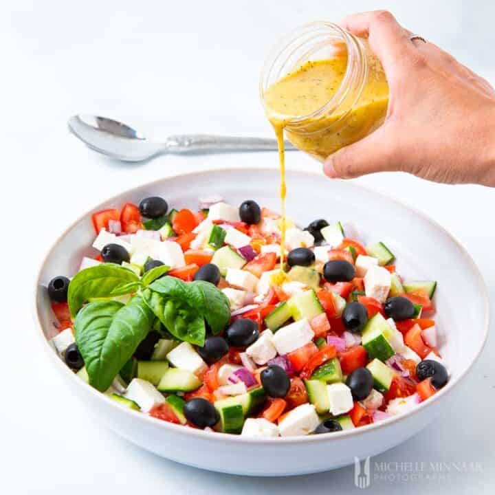 Jar of dressing being poured on a Mediterranean Salad