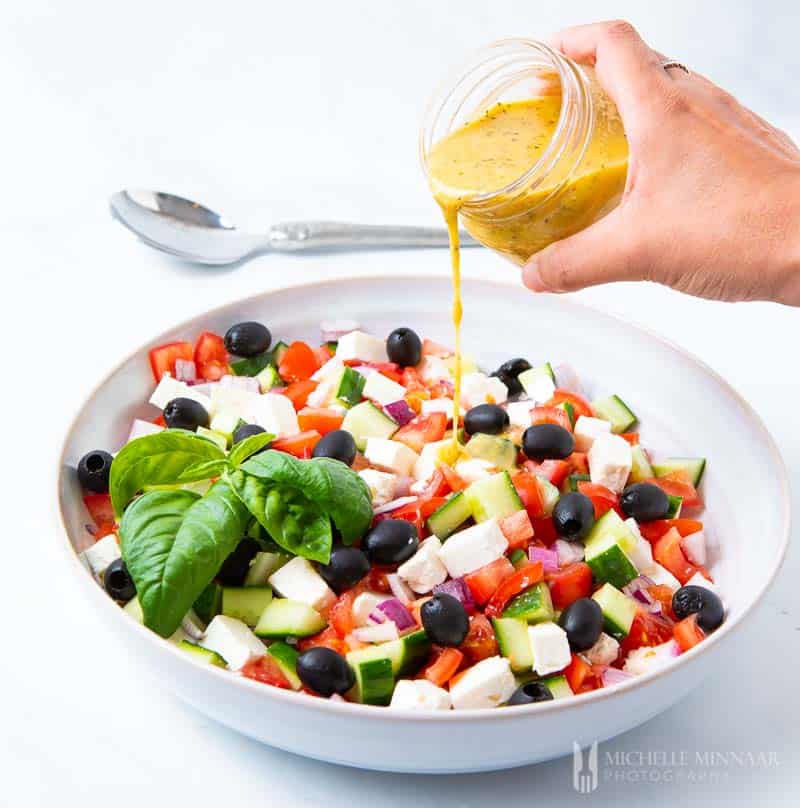 Jar of dressing being poured on a Mediterranean Salad