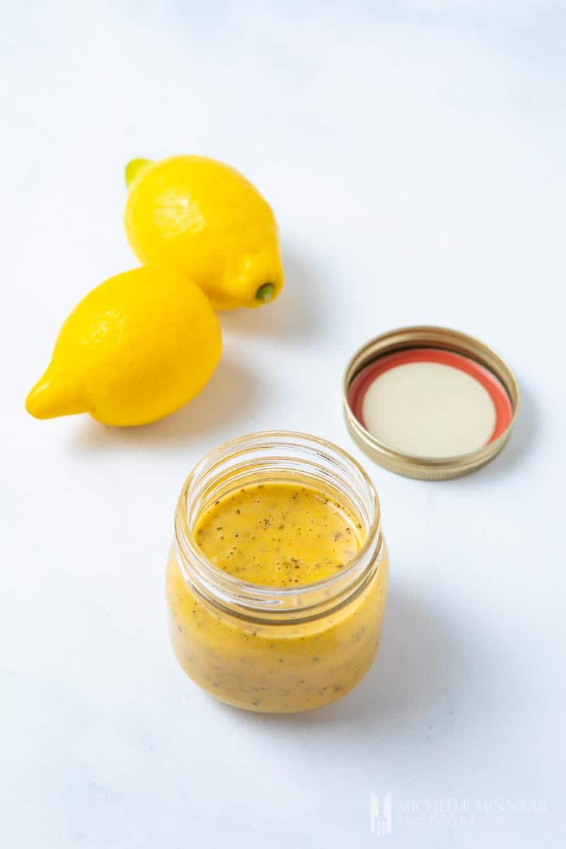 Two lemons and a clear glass jar of yellow Mediterranean Salad Dressing