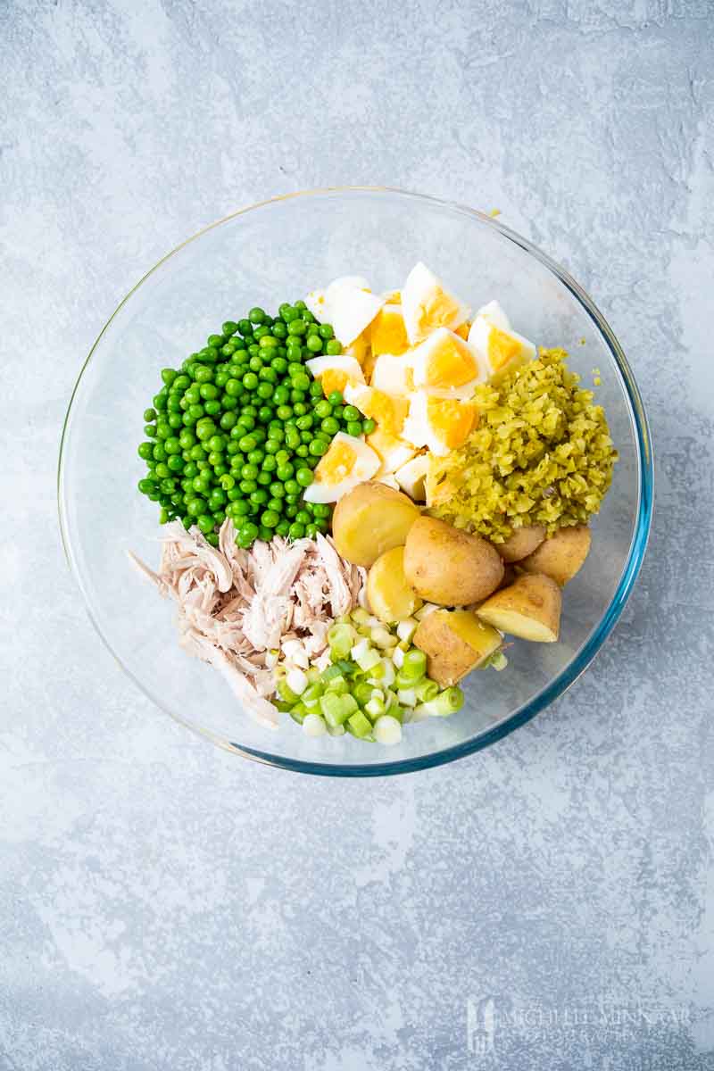 The ingredients for salad olivieh cut up in large glass bowl 