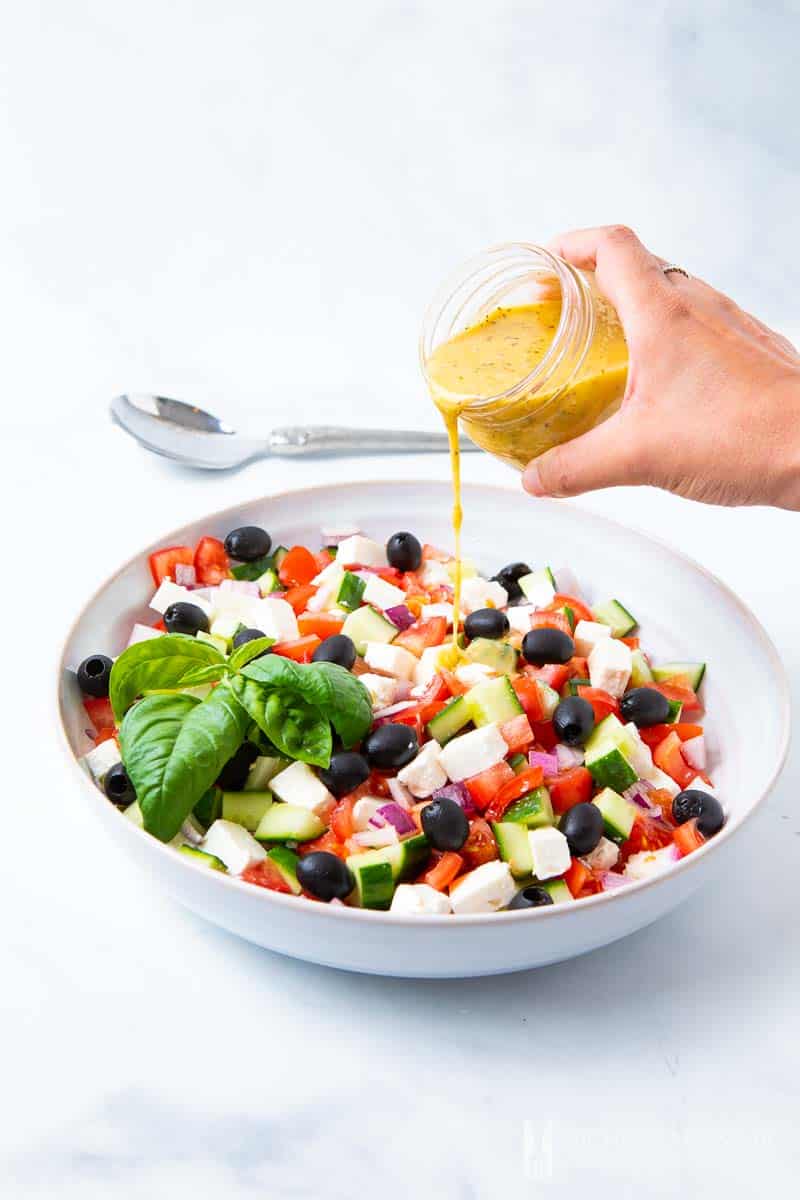 Mediterranean Salad Dressing being poured onto a colorful greek salad