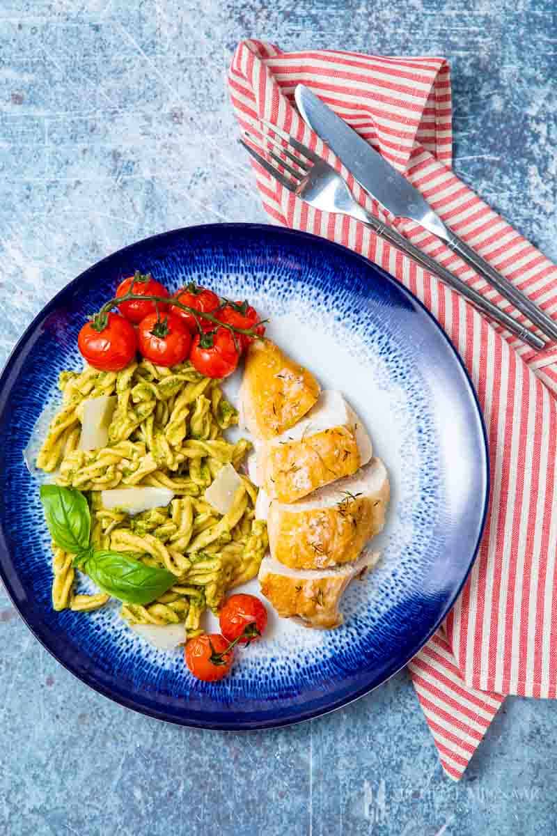 A plate of chicken pesto pasta, chicken breast, pasta with a green sauce