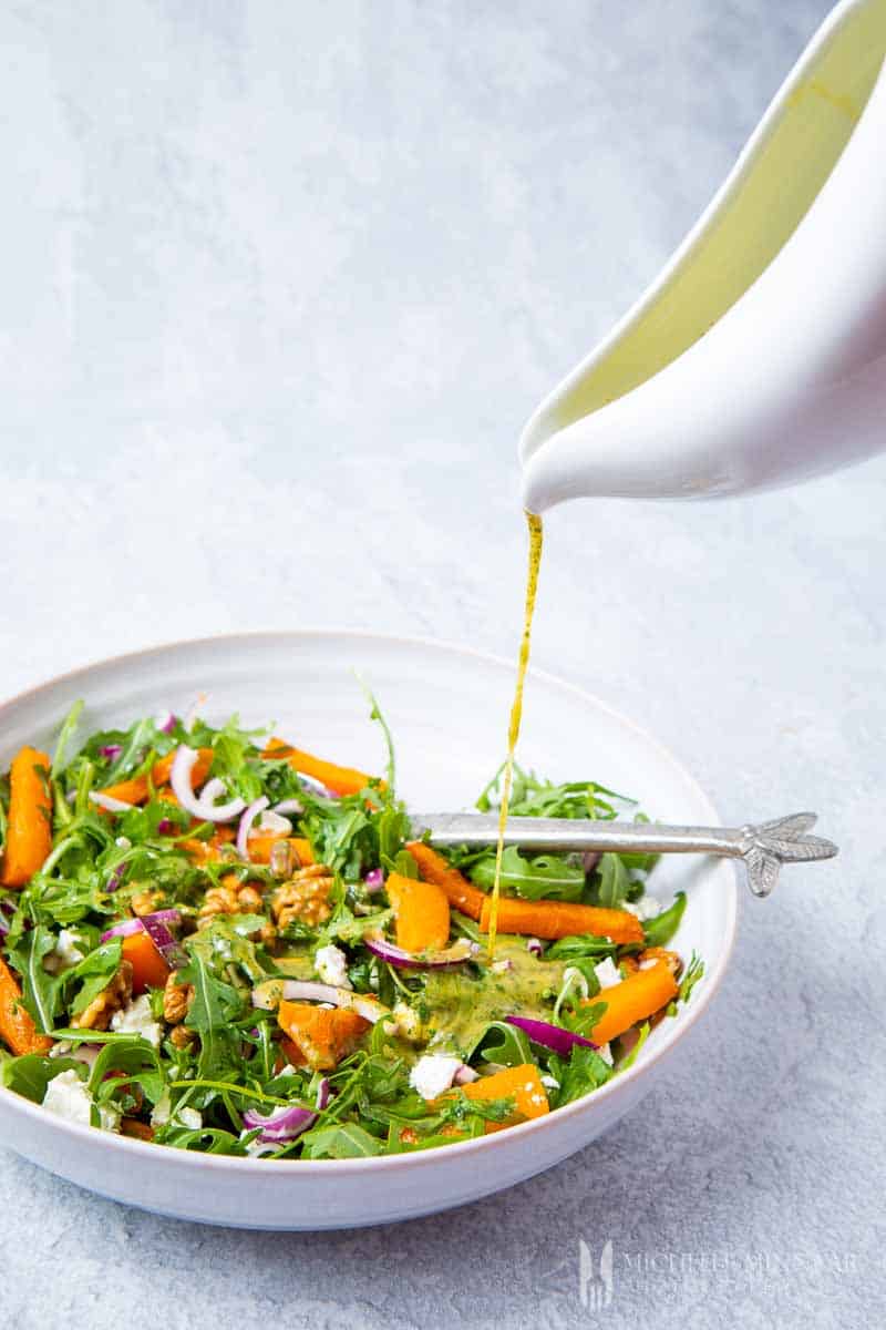 Salad dressing being poured into a bowl of salad 