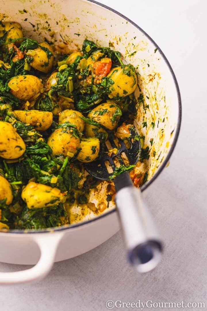 Bowl of saag aloo with a serving spoon.