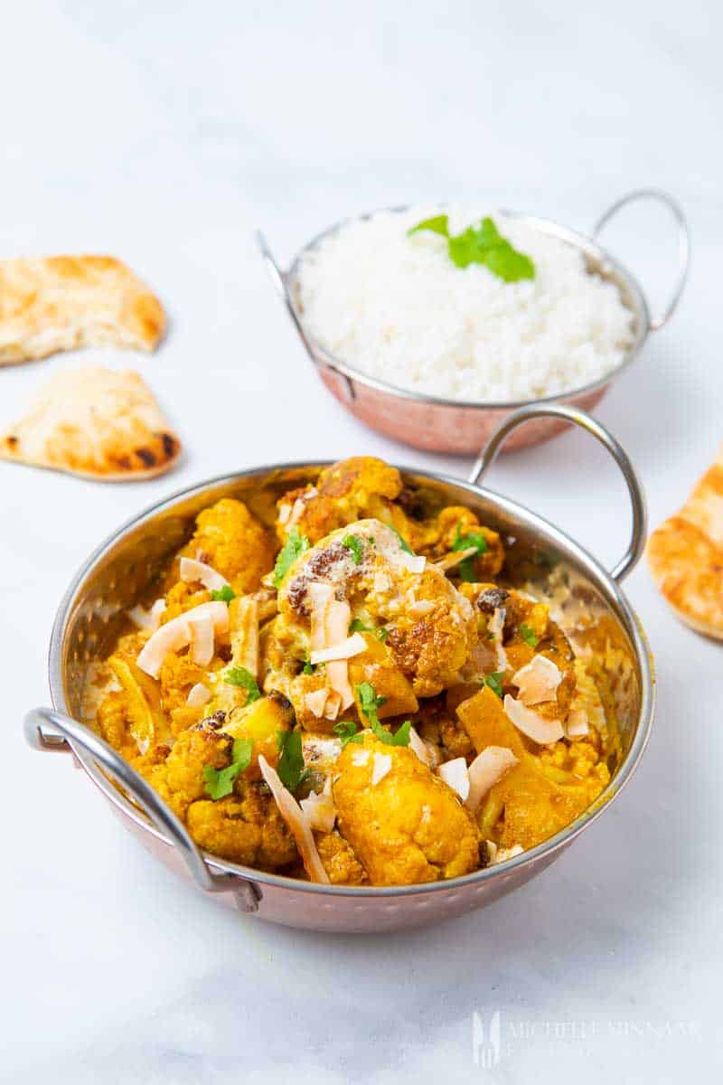 A bowl of cauliflower kurma with a bowl of rice