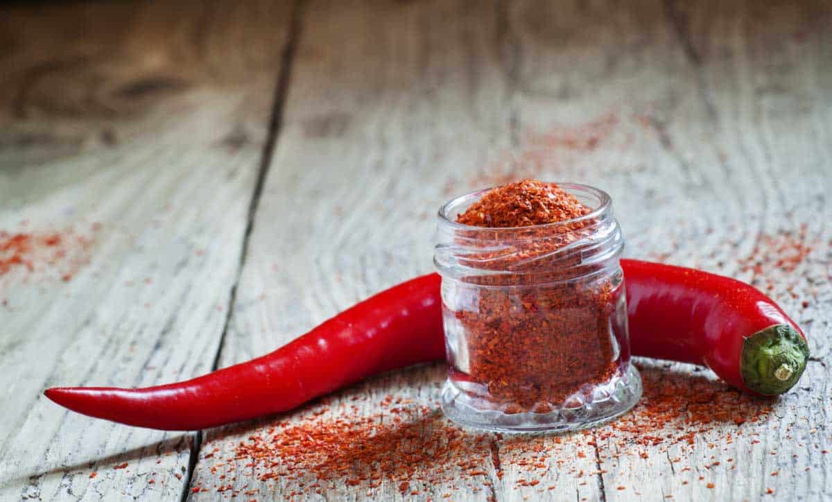 A glass jar of cayenne pepper and a fresh pepper.