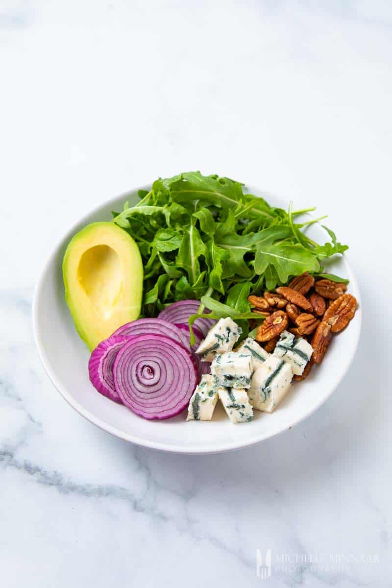 A close up of an avocado, onions, feta cheese and walnuts to make rocket salad