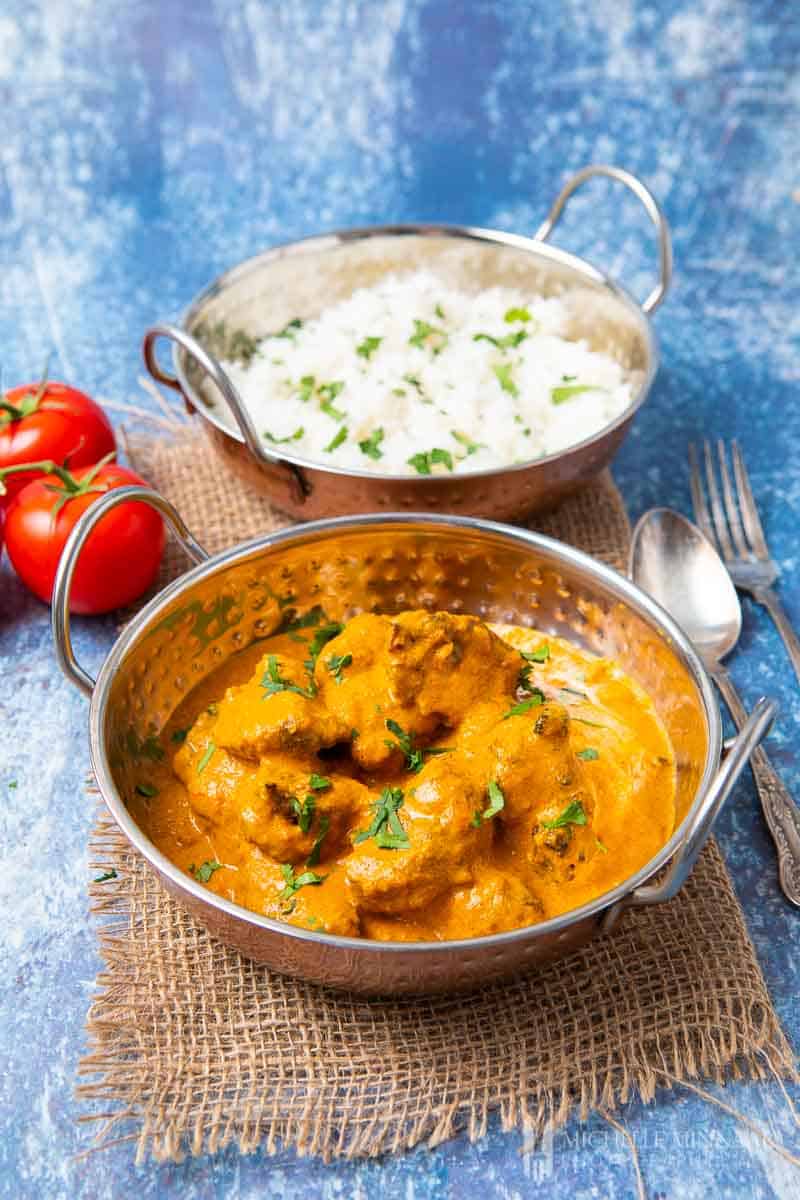 Close up of lamb in an orange sauce and a bowl of white rice 