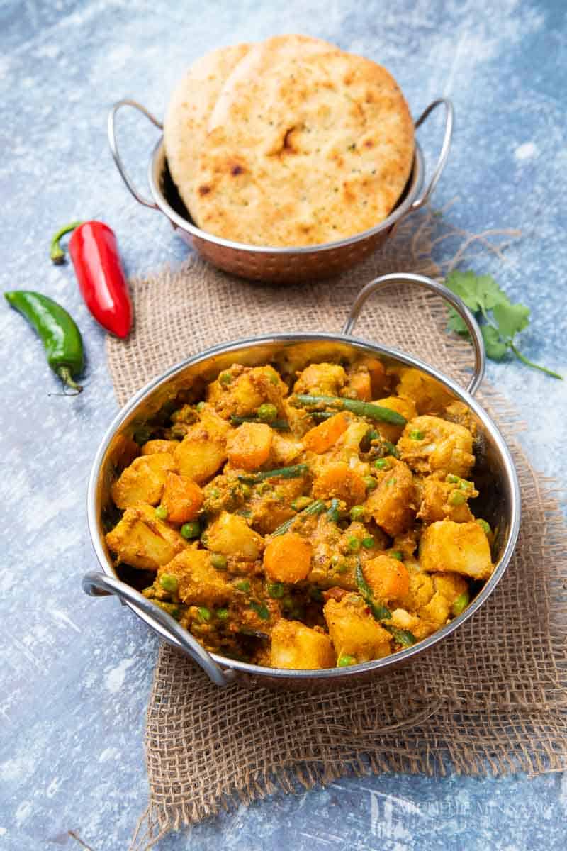 Bowl of yellow mixed vegetable curry and naan 