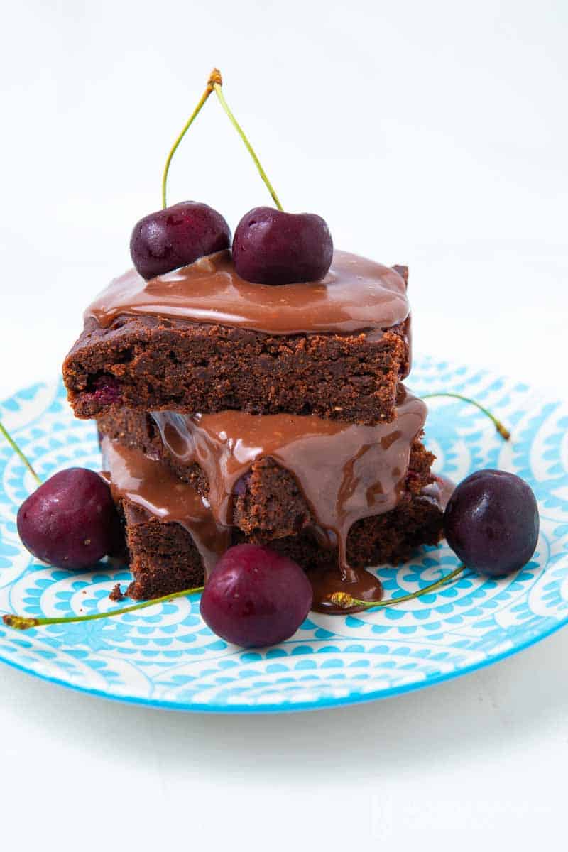 Two cherry brownies stacked on top of each other, covered in melted chocolate and fresh cherries