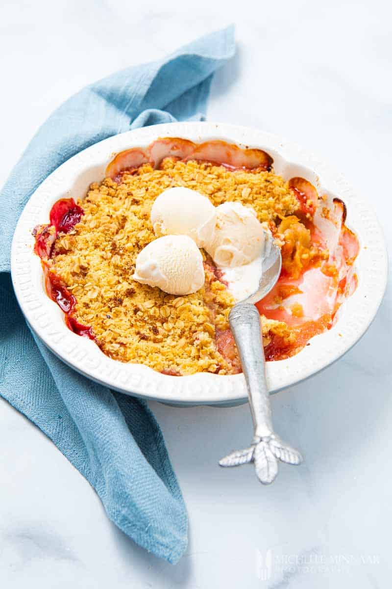 Plate of apple and plum crumble with three scoops of ice cream 