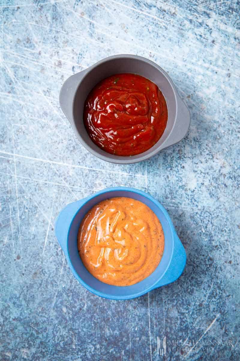 Two bowls of sauce, one red, one orange 