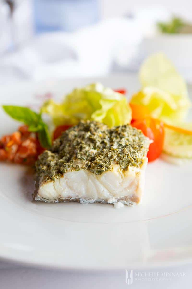 A close up of steamed cod with a green sauce