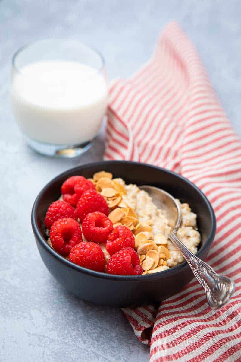 Bowl of almond milk porridge with fresh raspberries and a glass of milk