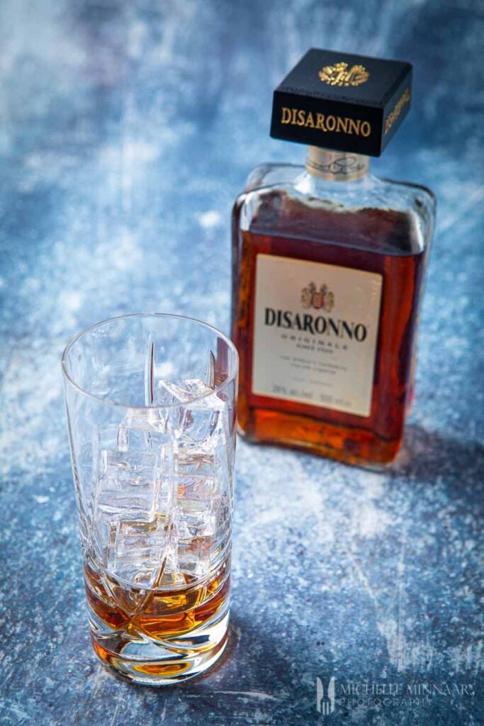Empty glass with ice and a bottle of amaretto