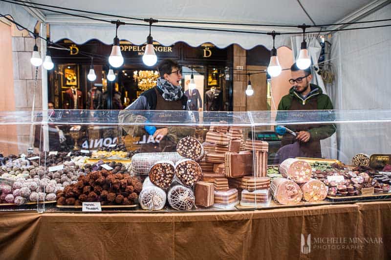 Chocolate salami displayed at chocolate stall with two attendants.