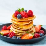 Tall stack of crempog with fresh berries and syrup