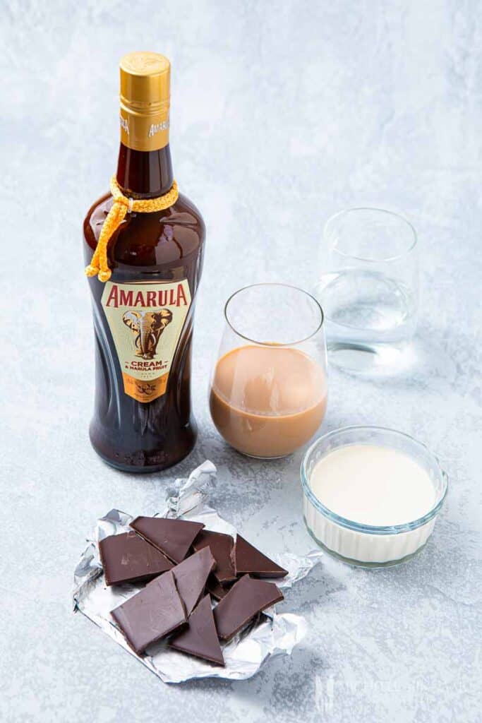 Bottle of Amarula, glass of tan liquid and chunks of chocolate