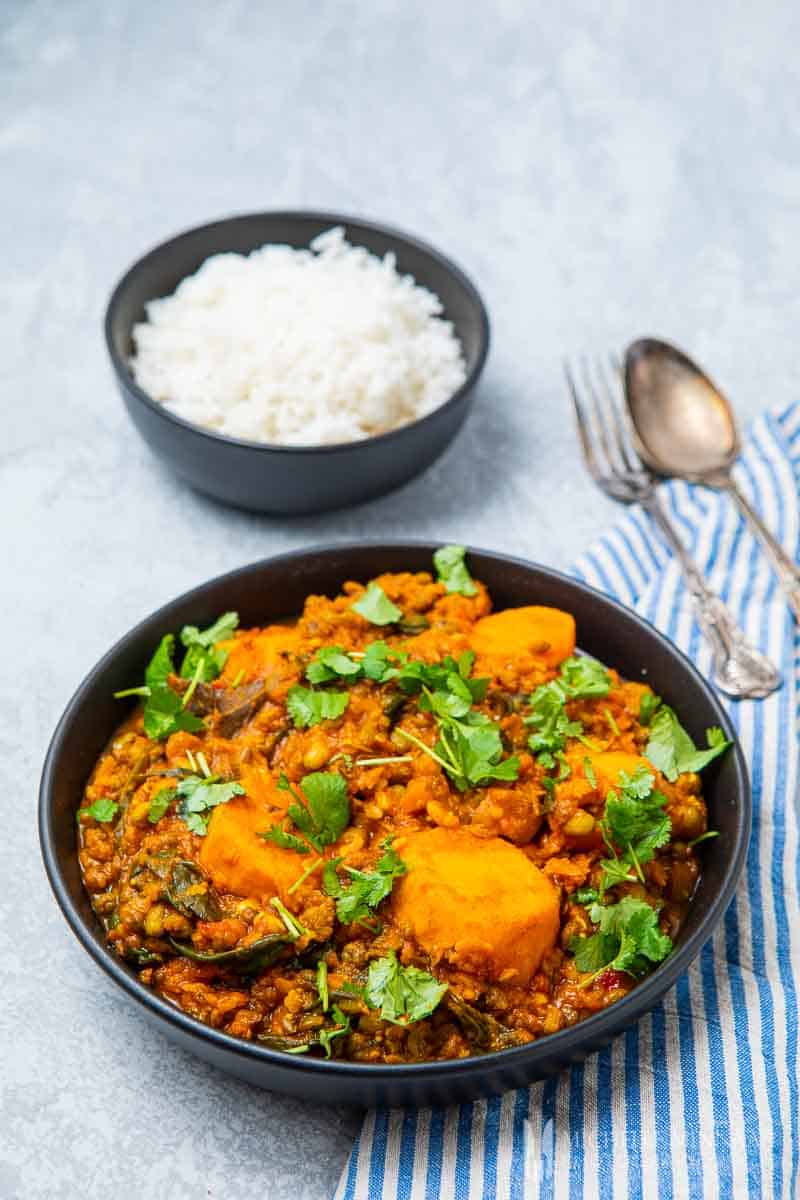 Bowl of vegan mung bean curry topped with parsley and side of rice