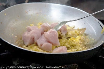 Raw chicken being added to a saucepan