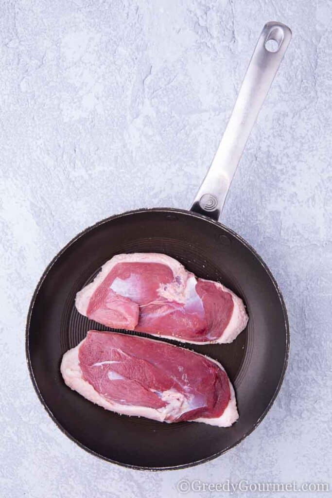 two raw duck breasts in pan