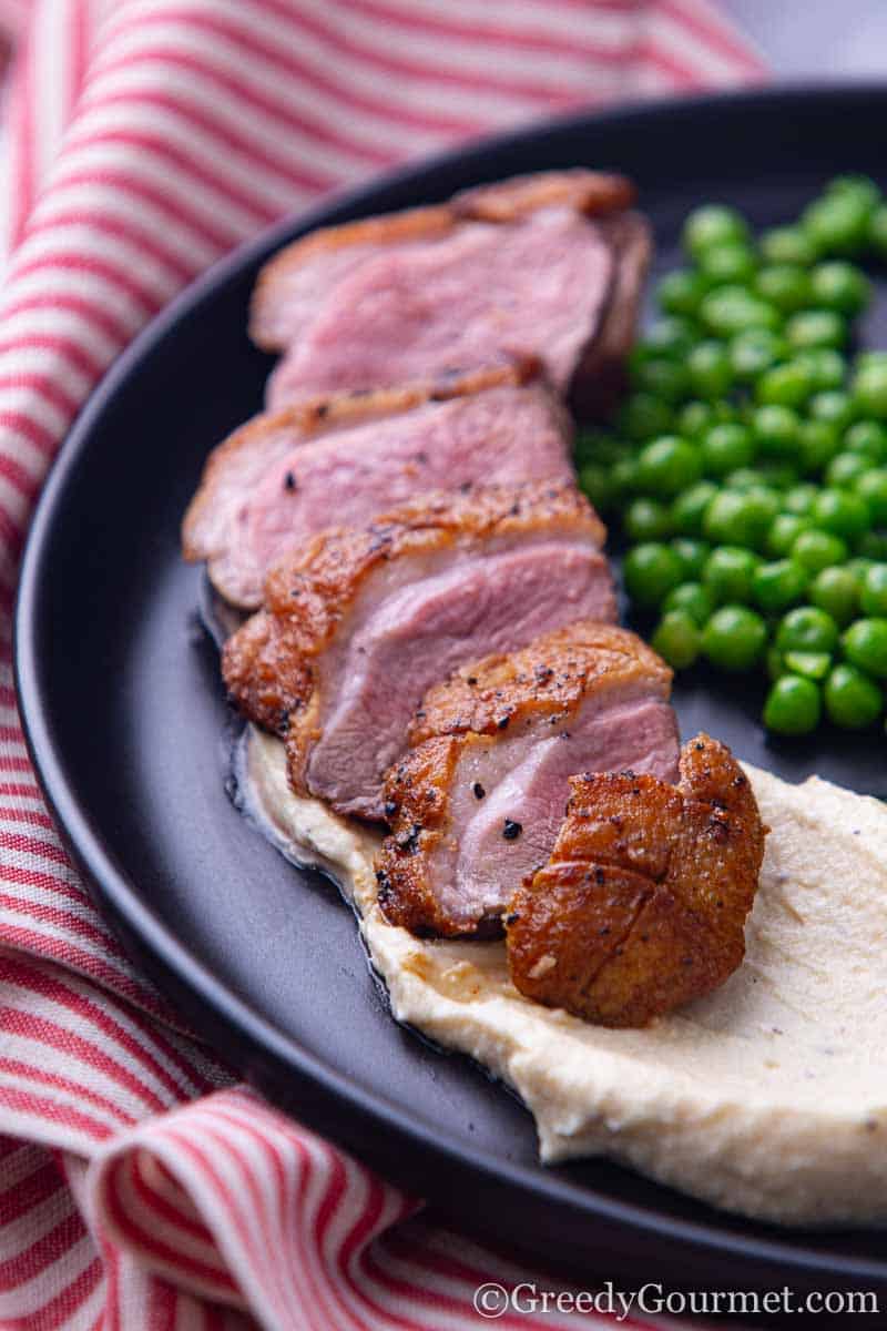 Sliced pan seared duck breast on a plate of mash potatoes