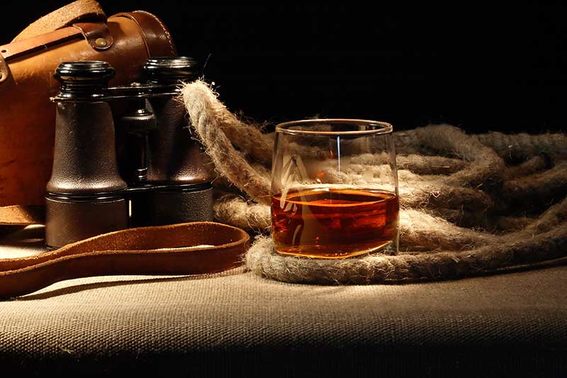 Half pour of brown rum with a rope and binoculars to be used as a cognac substitute