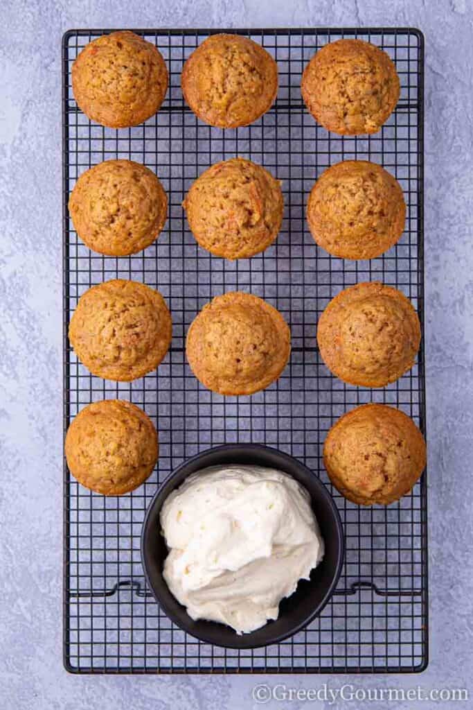Carrot cakes on drying rack with bowl of cream cheese frosting