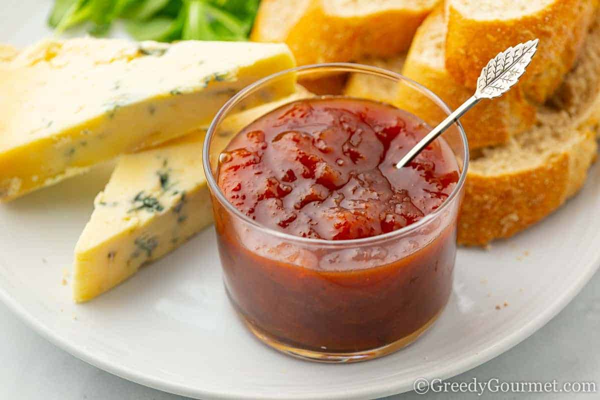 Short jar of apricot chutney with a leaf spoon and slices of blue cheese.