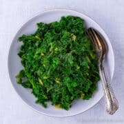 Fresh bowl of bright green kale with fork and spoon.