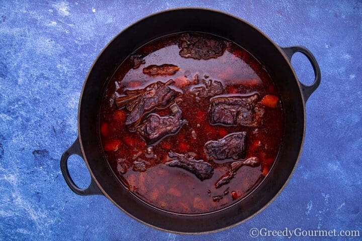 Braised short ribs simmering in saucepan