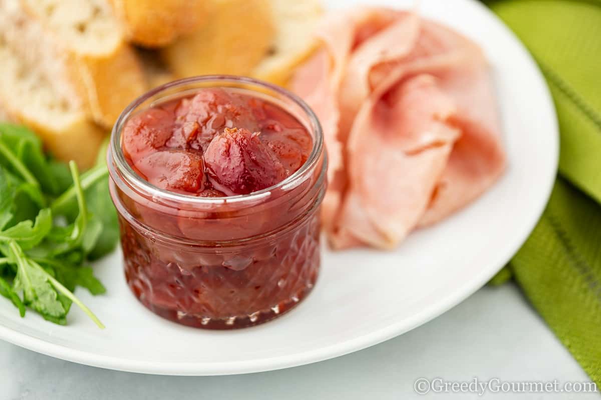 jar of red grape chutney served with bread and ham.