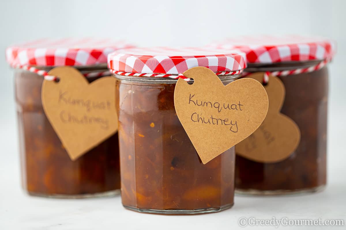 Three jars of kumquat chutney with red lids.