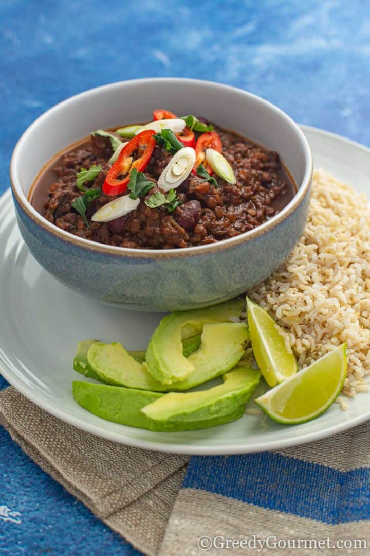 Burnt Aubergine Chilli with rice and slices of avocado served with lime slices