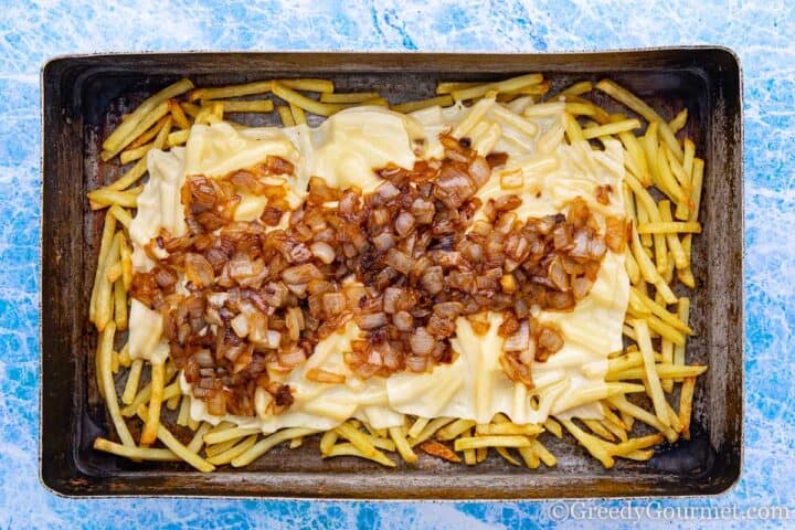 Baking tray full of fries, melted cheese and caramelised onions