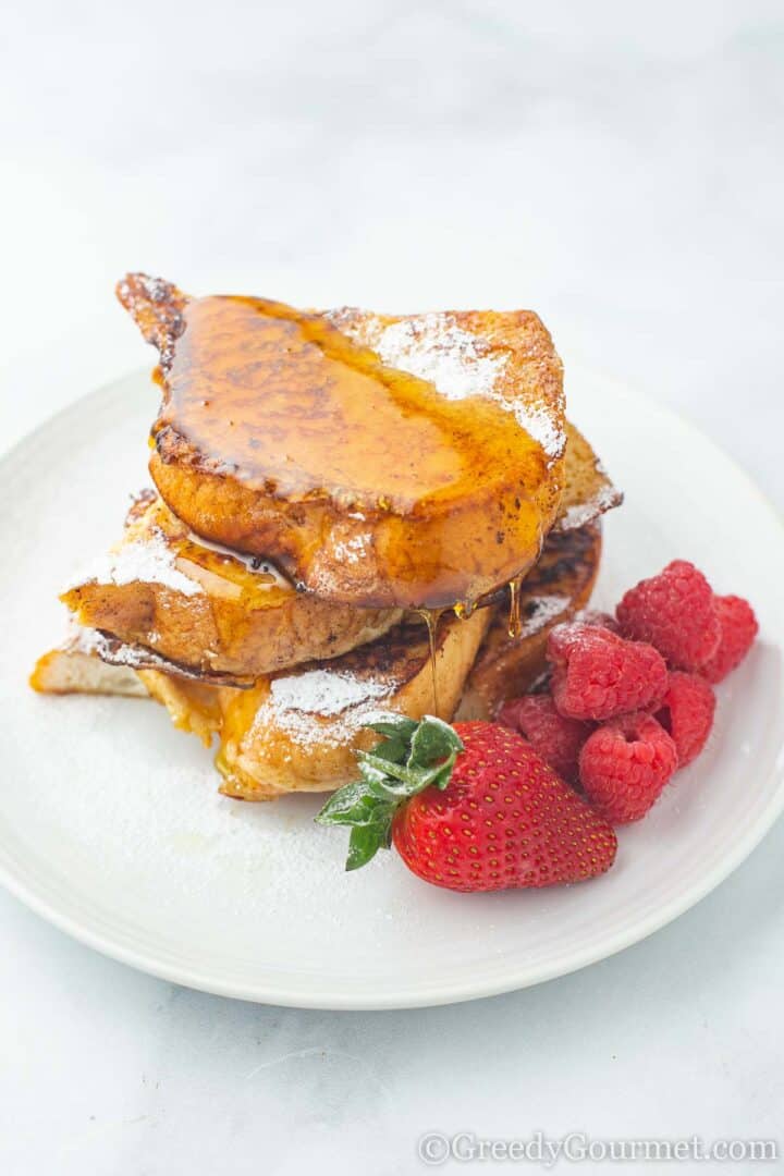 Eggnog French Toast covered in maple syrup with stawberries and raspberries