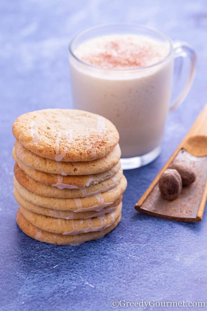 stacked eggnog cookies with a glass of eggnog.