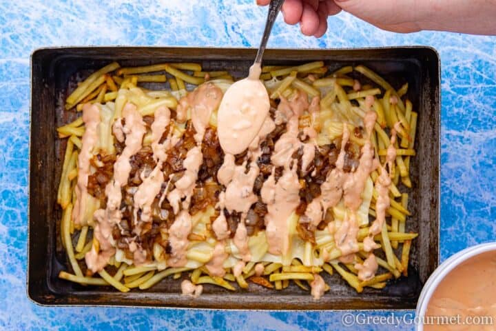 Spooning in-and-out sauce over the baking tray of ingredients 