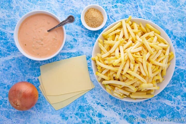 Bowl of uncooked fries alongside cheese slices, onion, in-and-out sauce and salt.