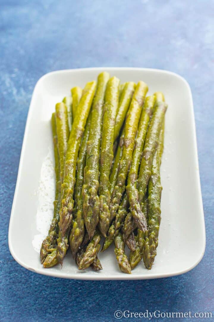 cooked asparagus on a white plate with salt