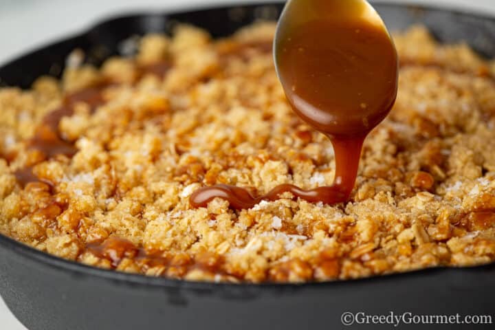 Crumble being topped with salted caramel sauce