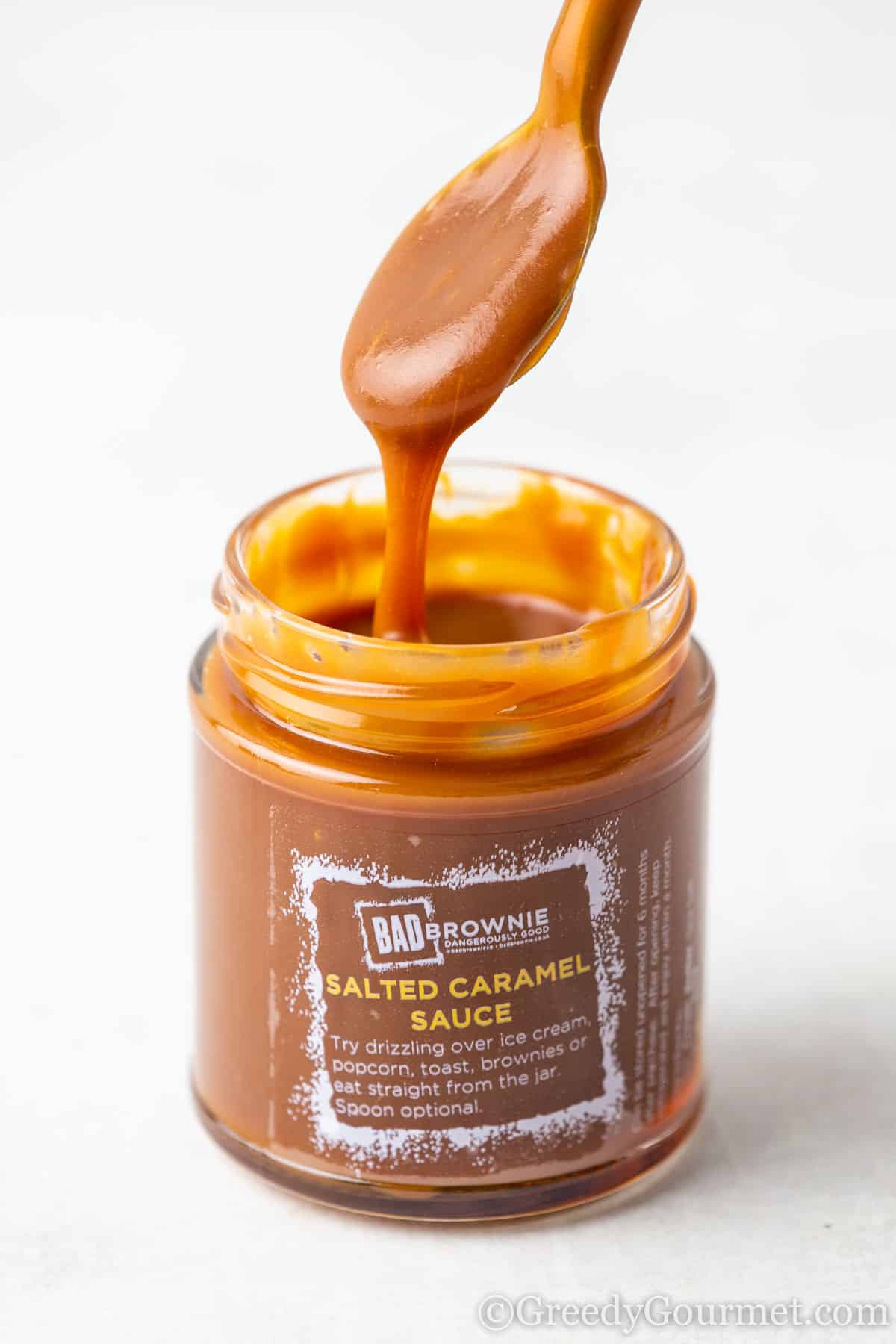 A jar of bad brownie salted caramel sauce with a wooden spoon