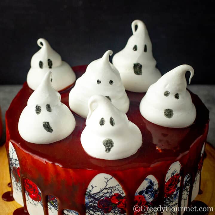 Six white meringue ghosts on top of a halloween cake