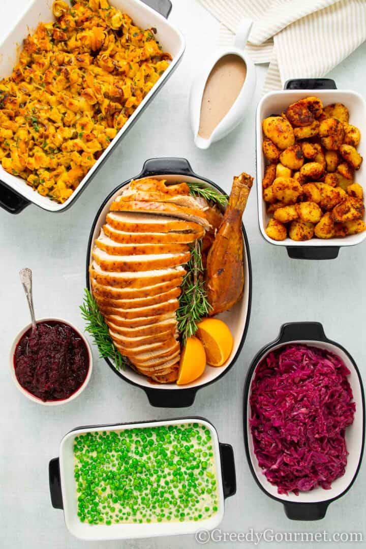 Recipes for a roast dinner laid on a table, turkey, cheesy peas, potatoes, slow cooker red cabbage.