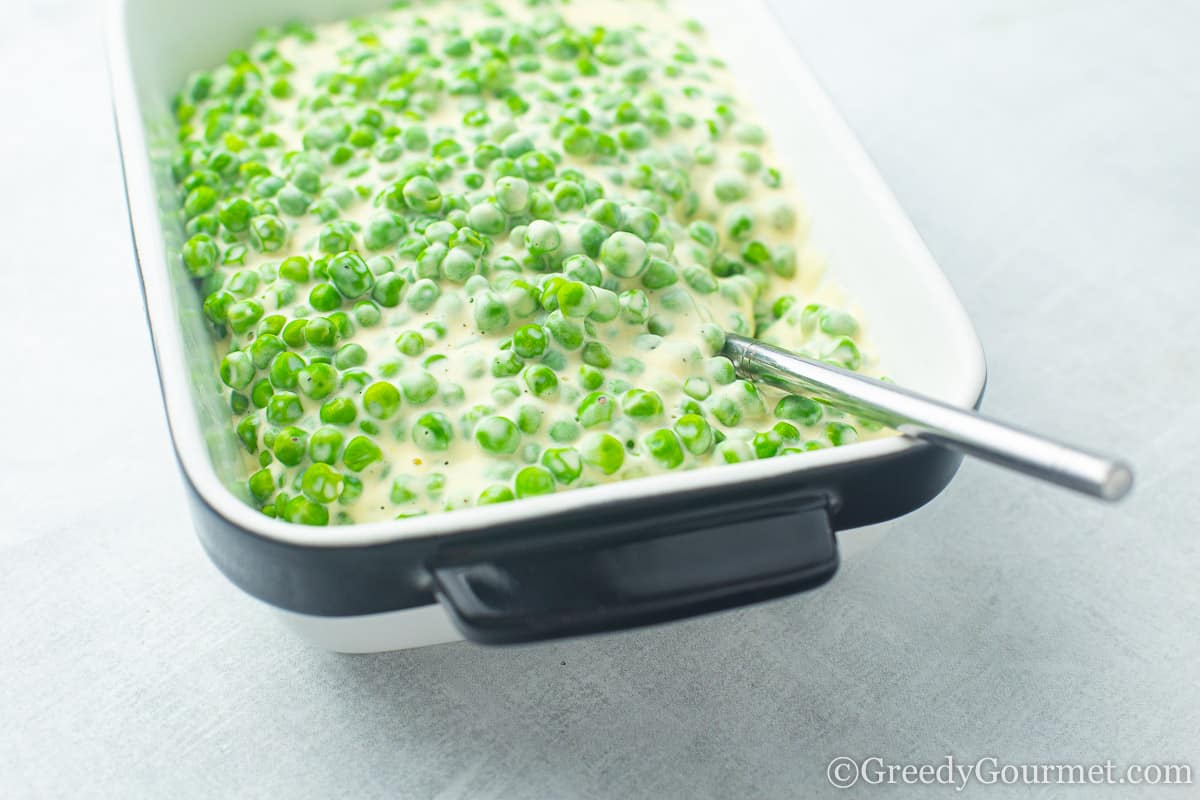 Baking dish full of greens peas and cheese sauce to show you how to cook peas